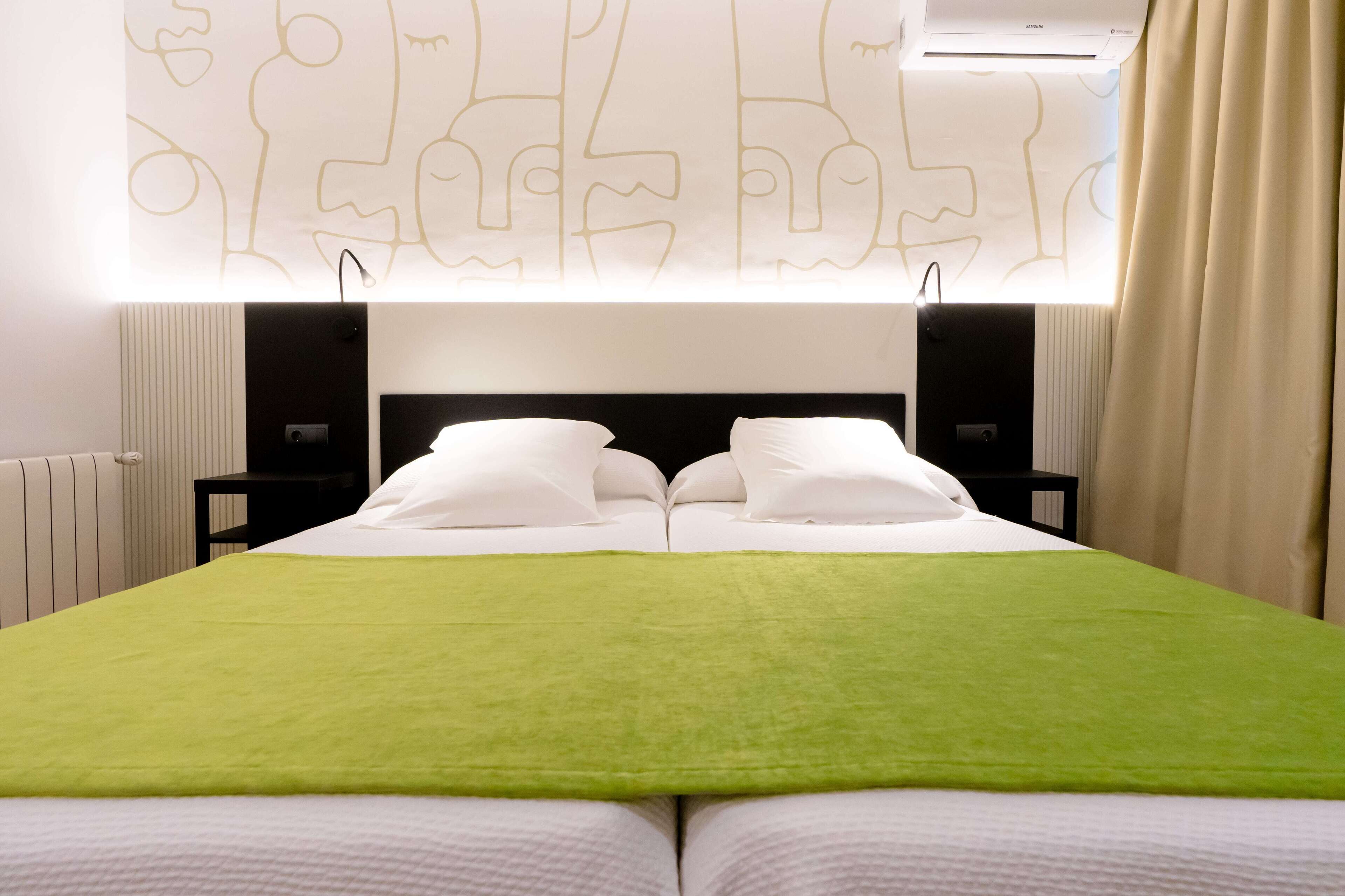 Une chambre d’hôtel avec un grand lit, deux tables de chevet, un climatiseur fixé au mur et une fenêtre avec des rideaux.