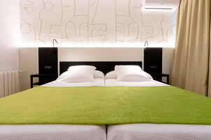 Camera d'albergo con un letto grande, due comodini, condizionatore d'aria a parete e una finestra con tende.