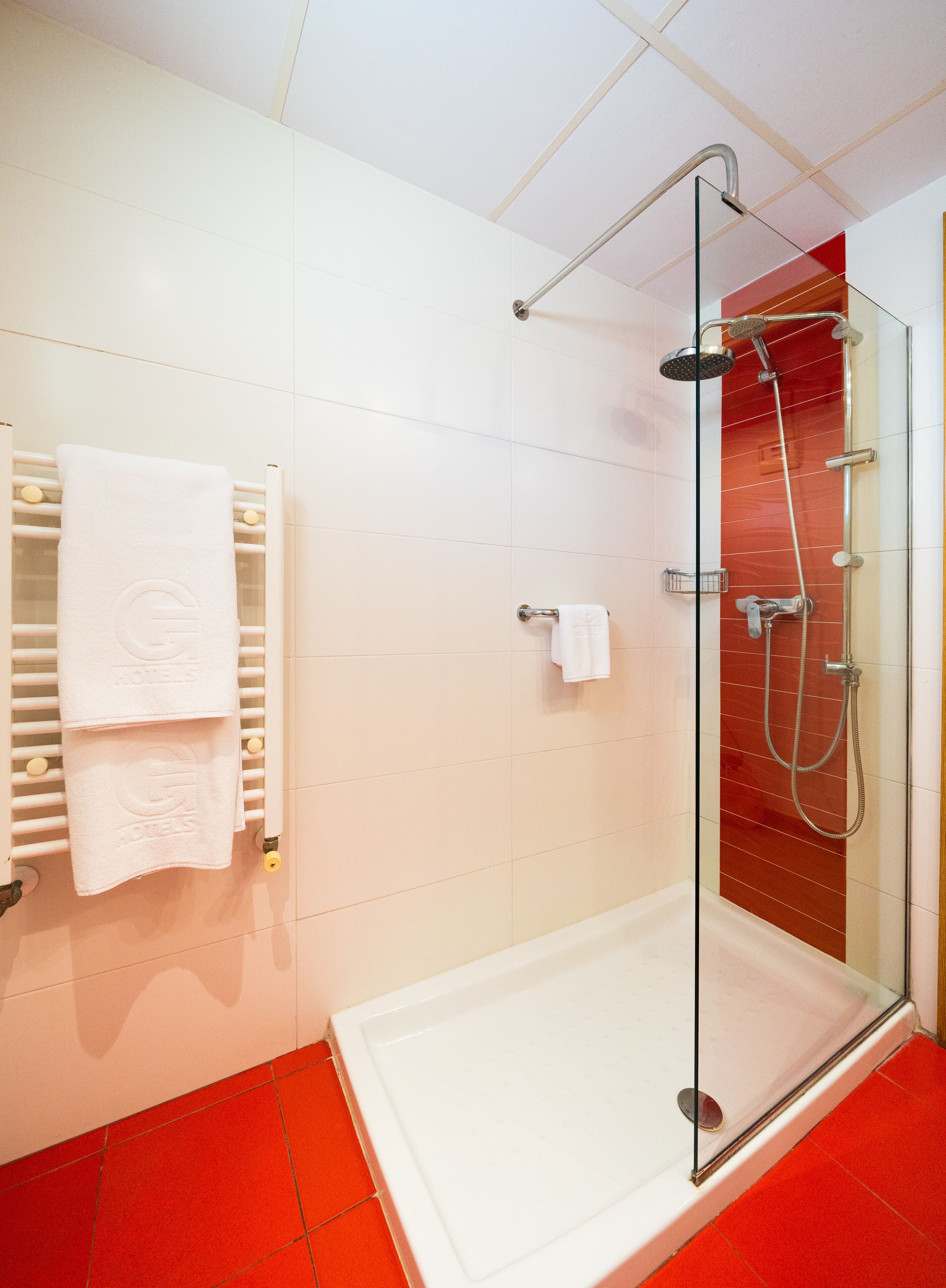 Un baño moderno con ducha envuelta en vidrio, paredes de azulejos blancos y suelo de baldosas rojas.