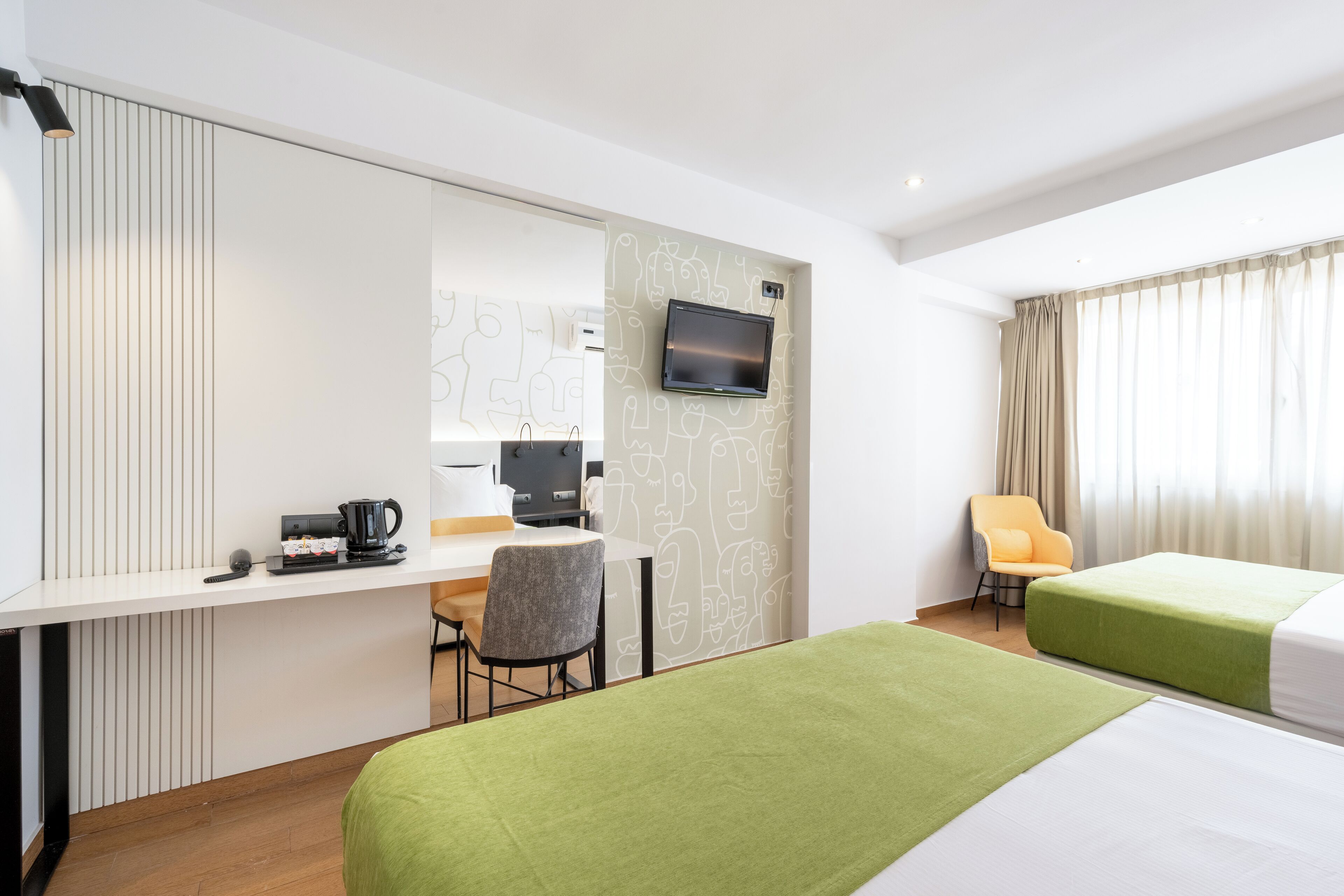 Une chambre d’hôtel avec deux lits, un bureau avec un ordinateur, une chaise et un téléviseur fixé au mur.