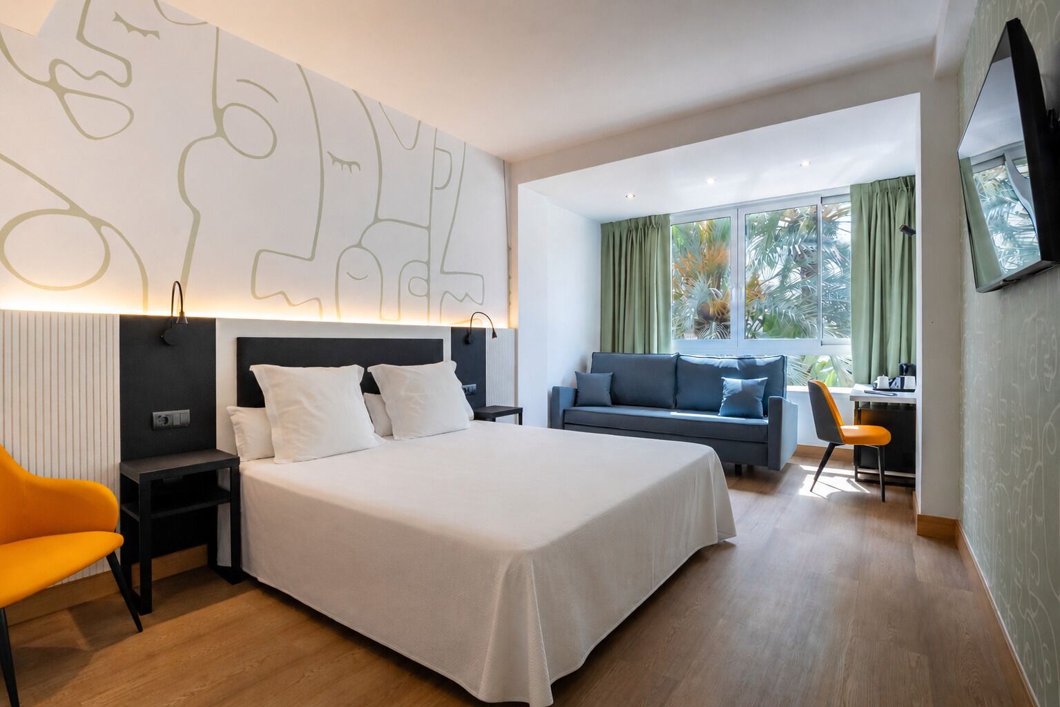 A modern hotel room with a large bed, a desk, a sofa, and a TV.