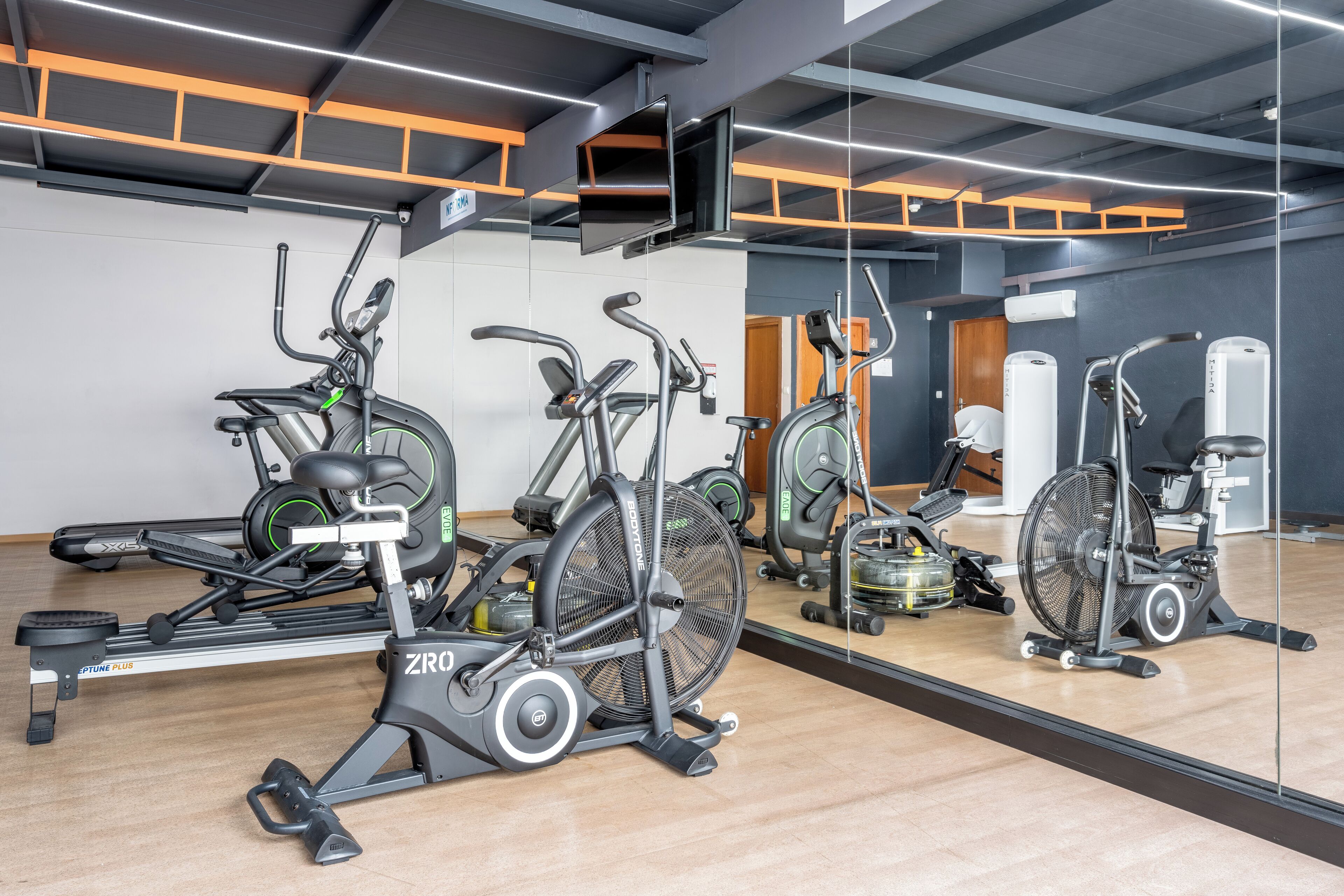 Ein Fitnessraum mit Ergometerbikes, Laufbändern und einer Spiegelwand.
