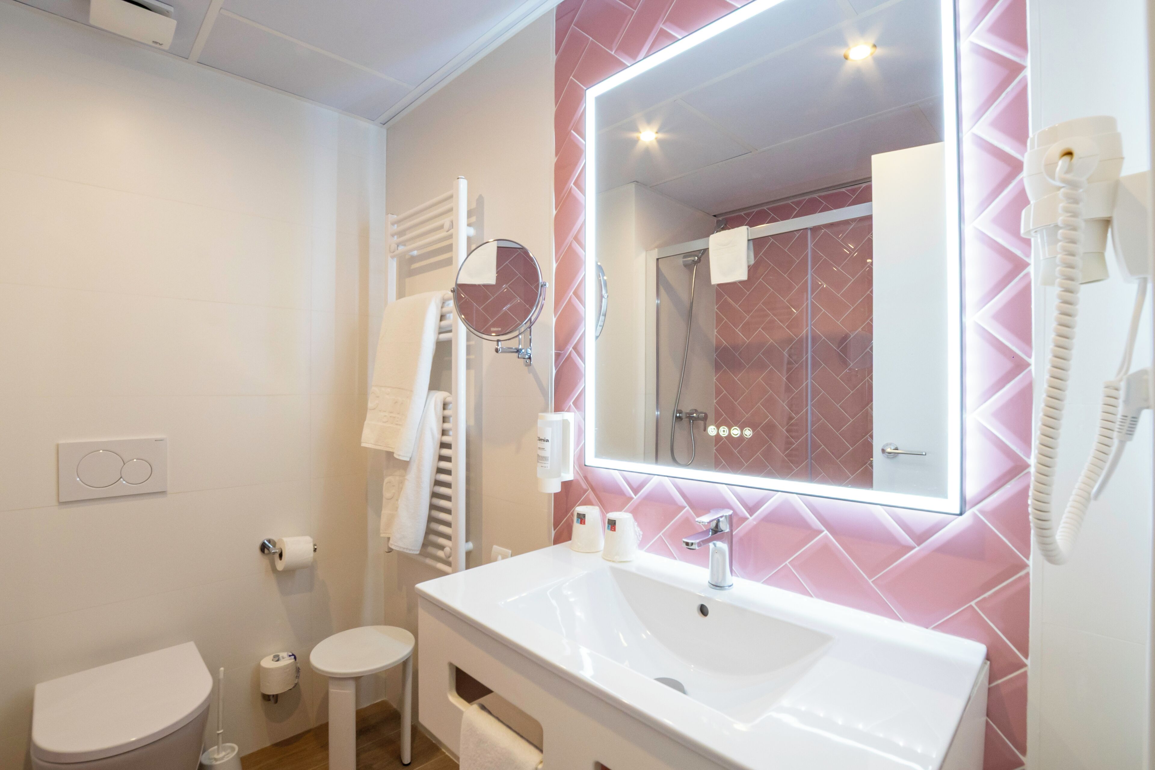 A modern bathroom with a white sink, a large mirror, and a pink tiled wall.