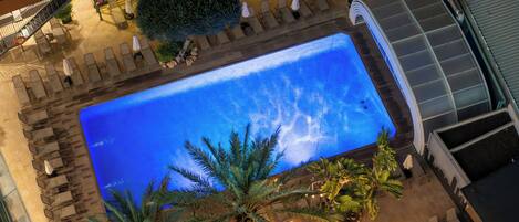 Vista aérea de una zona de piscina hotelera con tumbonas y palmeras.