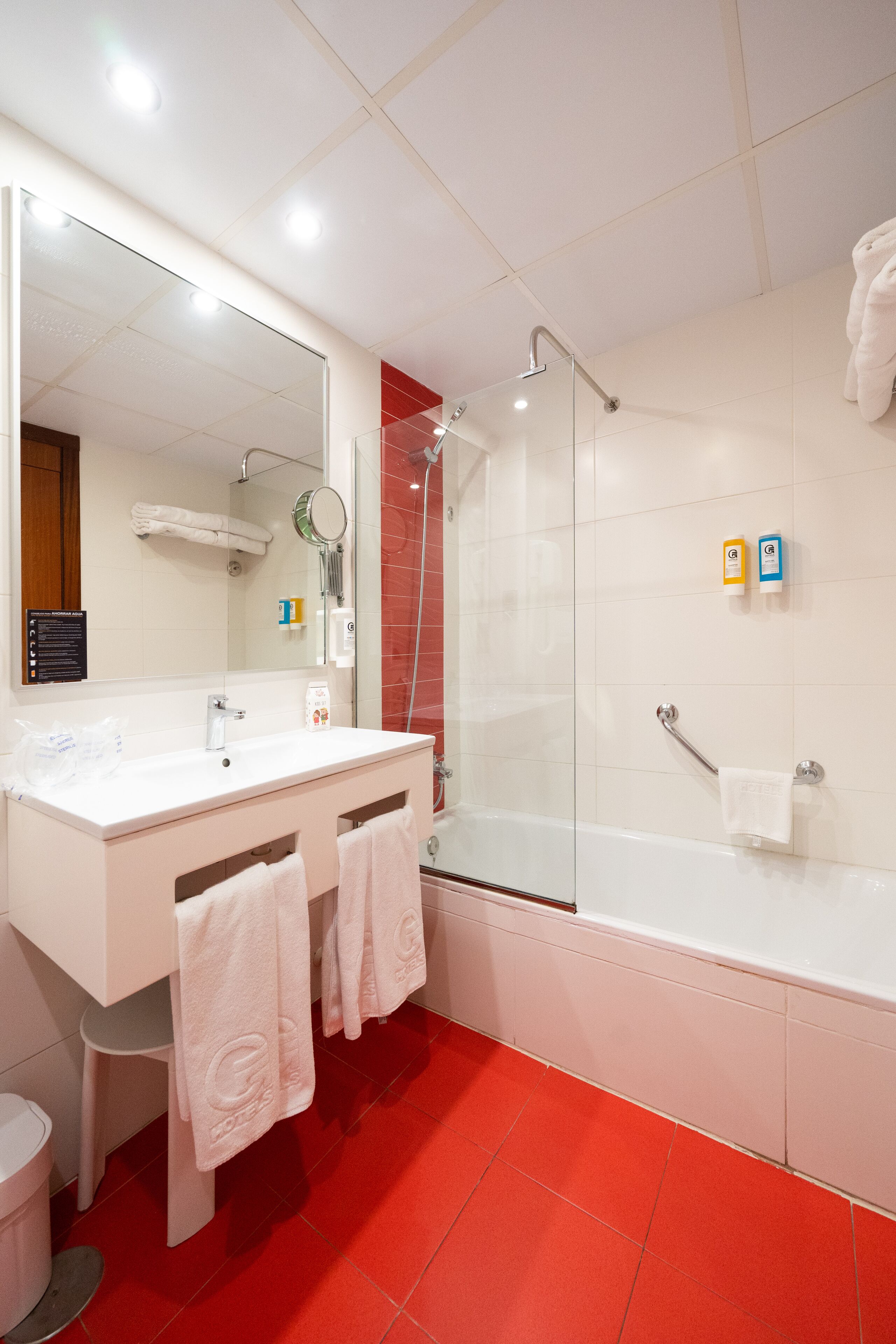 Een moderne badkamer met een witte wastafel, een douche met glazen wanden en rood betegelde vloer.