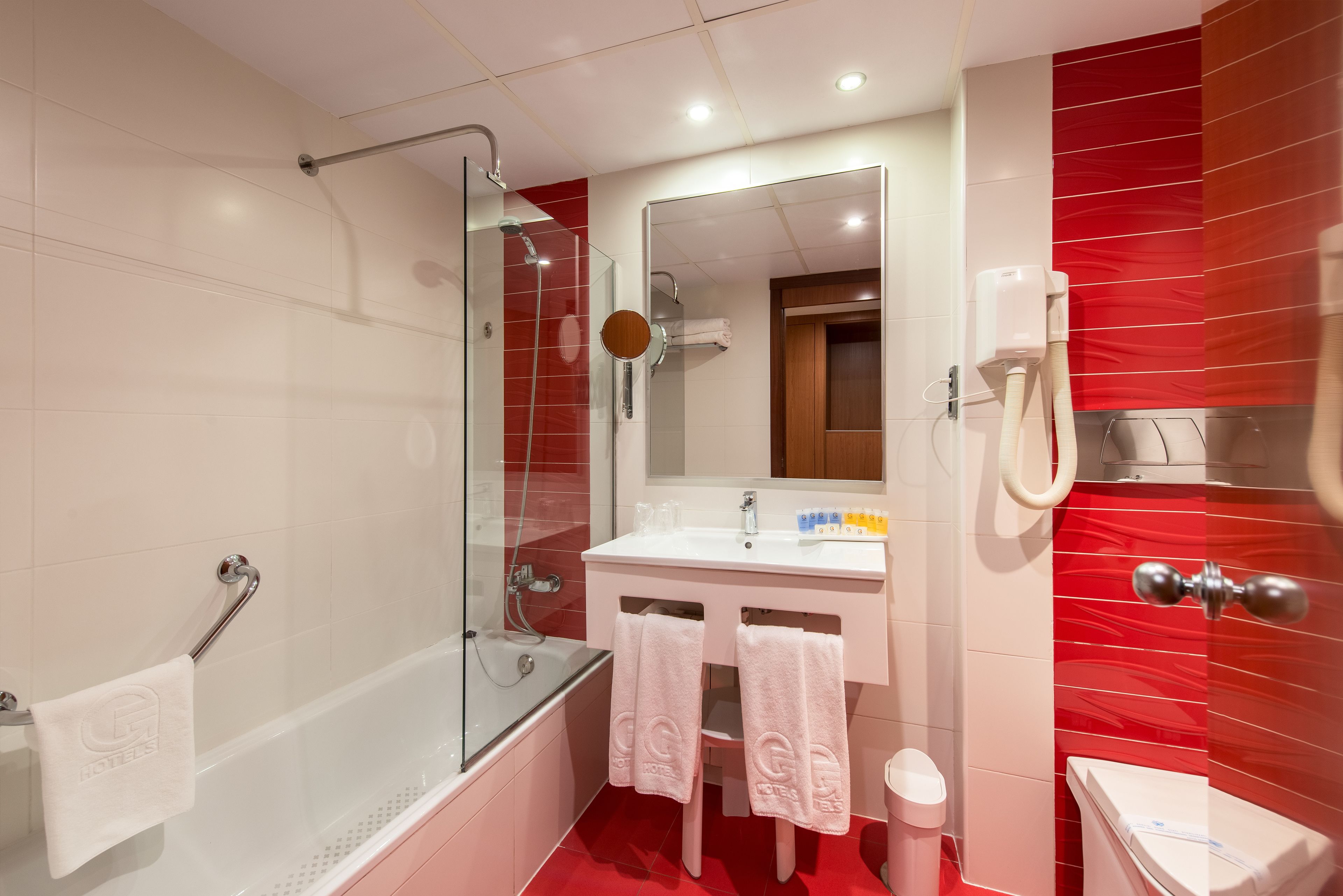 A modern bathroom with a glass-enclosed shower, a white sink, and a red-tiled wall.