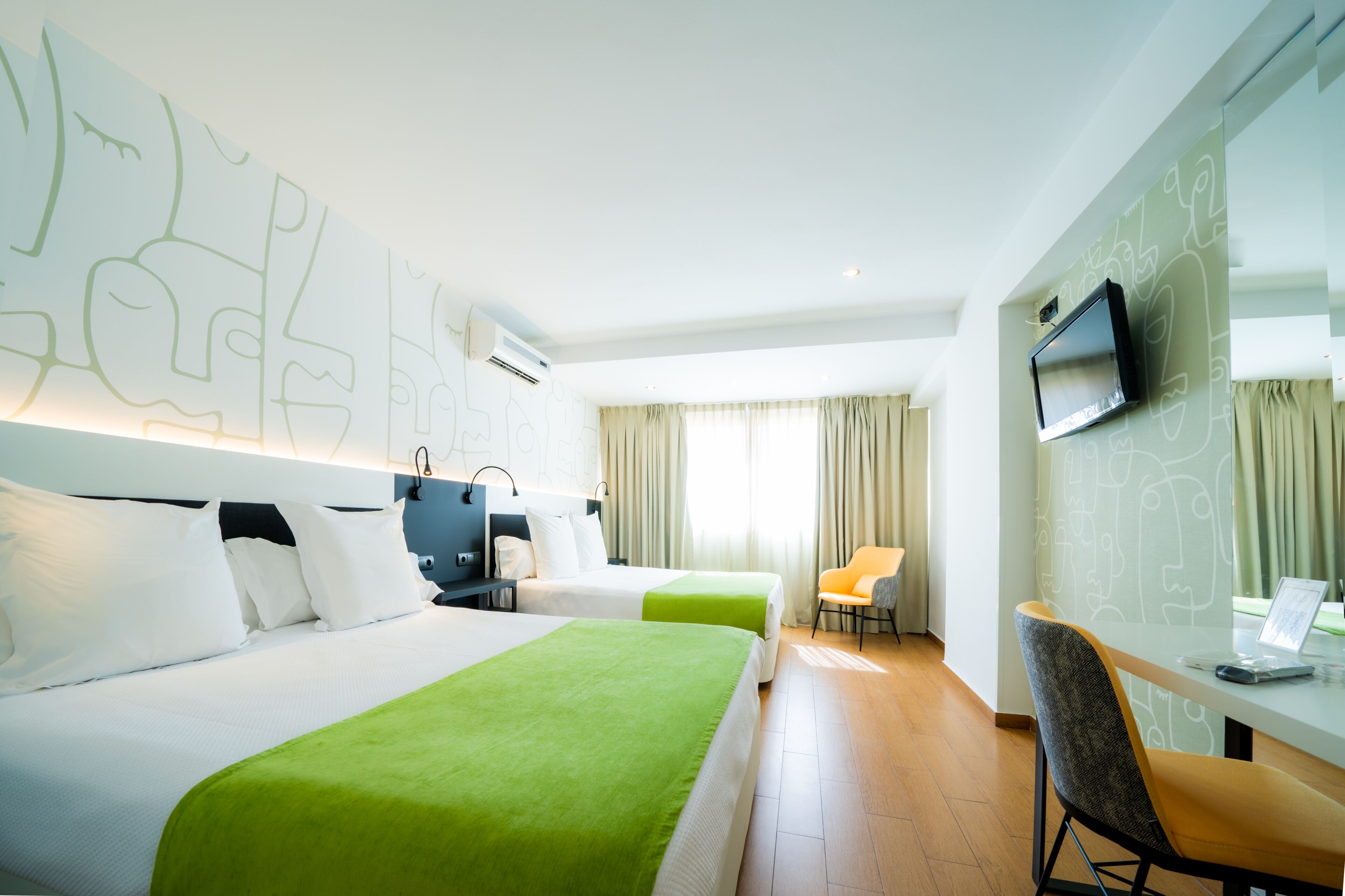 A hotel room with two beds, a desk with a laptop, a TV, and a chair.