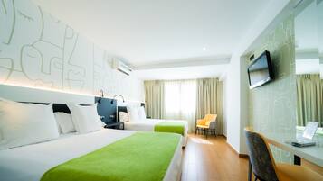 A hotel room with two beds, a desk with a laptop, a TV, and a chair.
