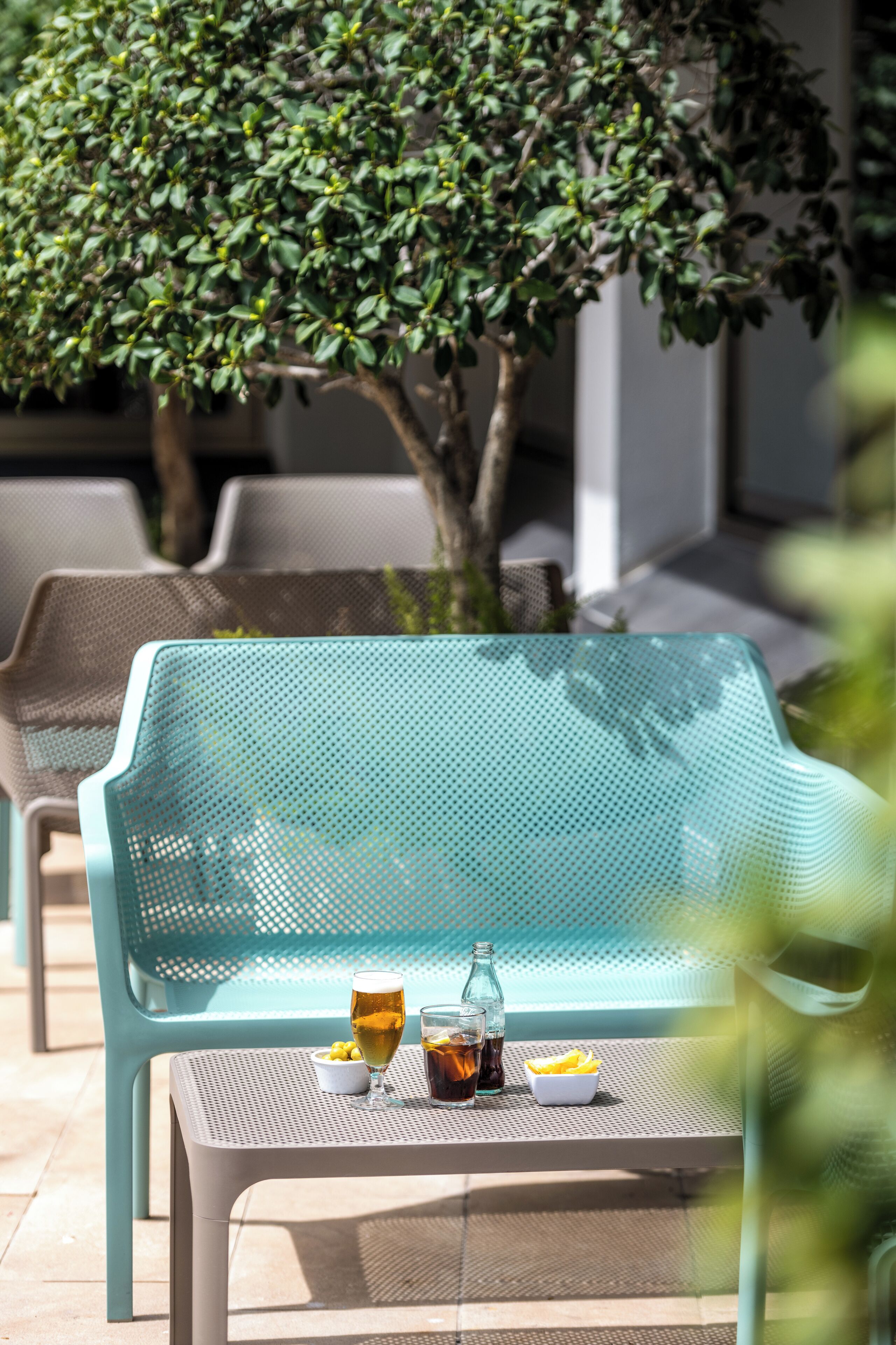 A turquoise metal chair with a table, a glass of beer, and a bottle of soda.