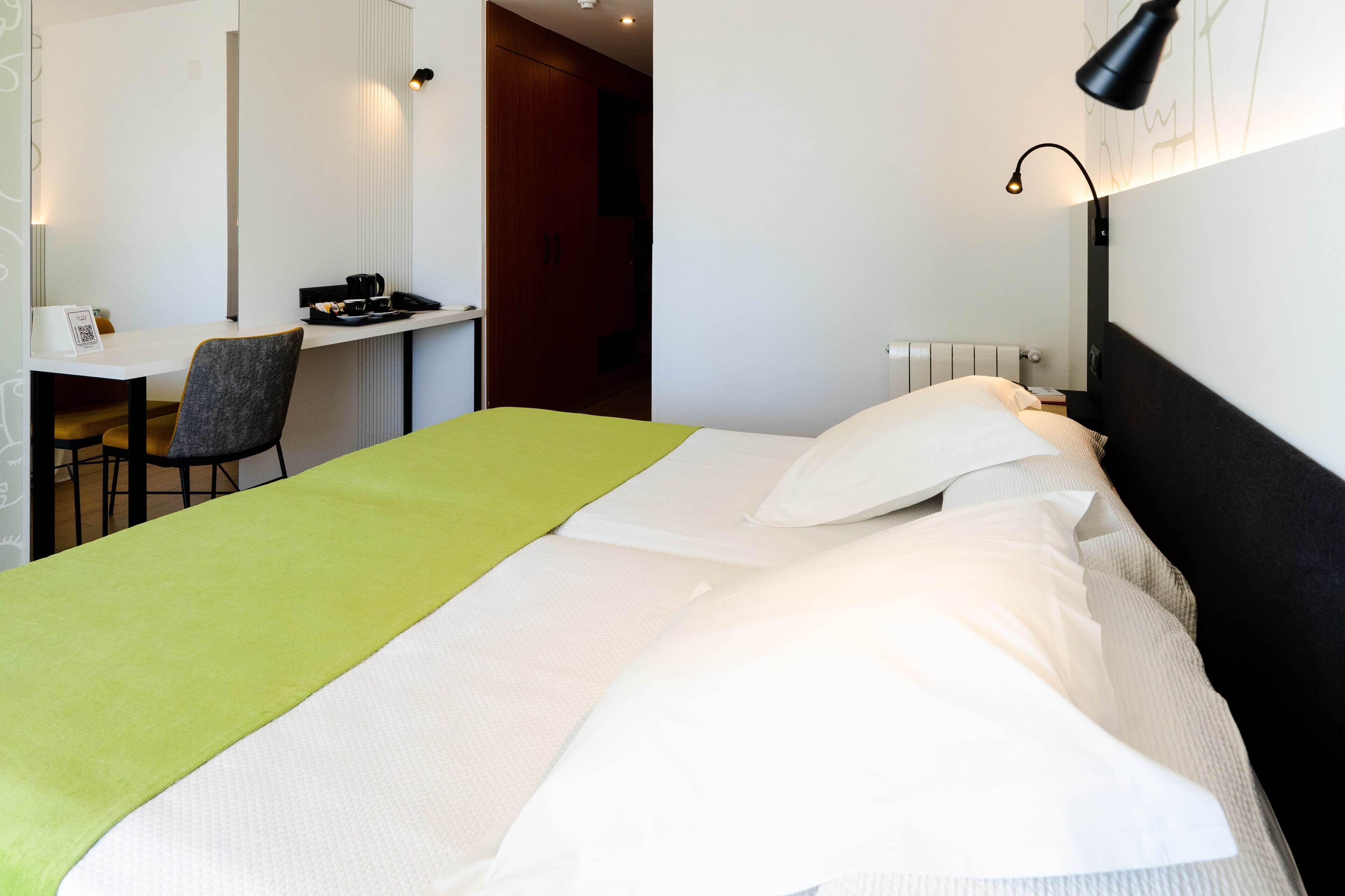 A hotel room with a bed, a desk, a chair, and a nightstand.