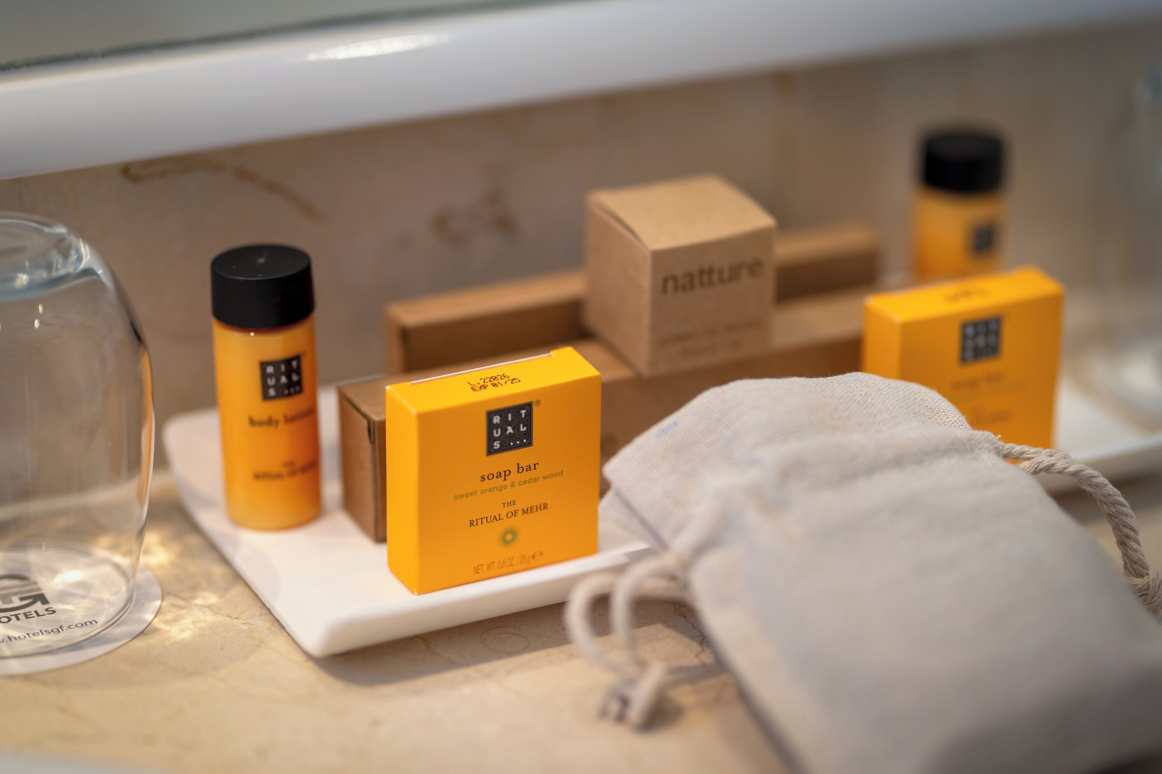 Een badkamerplank met diverse toiletartikelen, waaronder een zeepstaafje, een fles en een doosje met de tekst 'natture'.