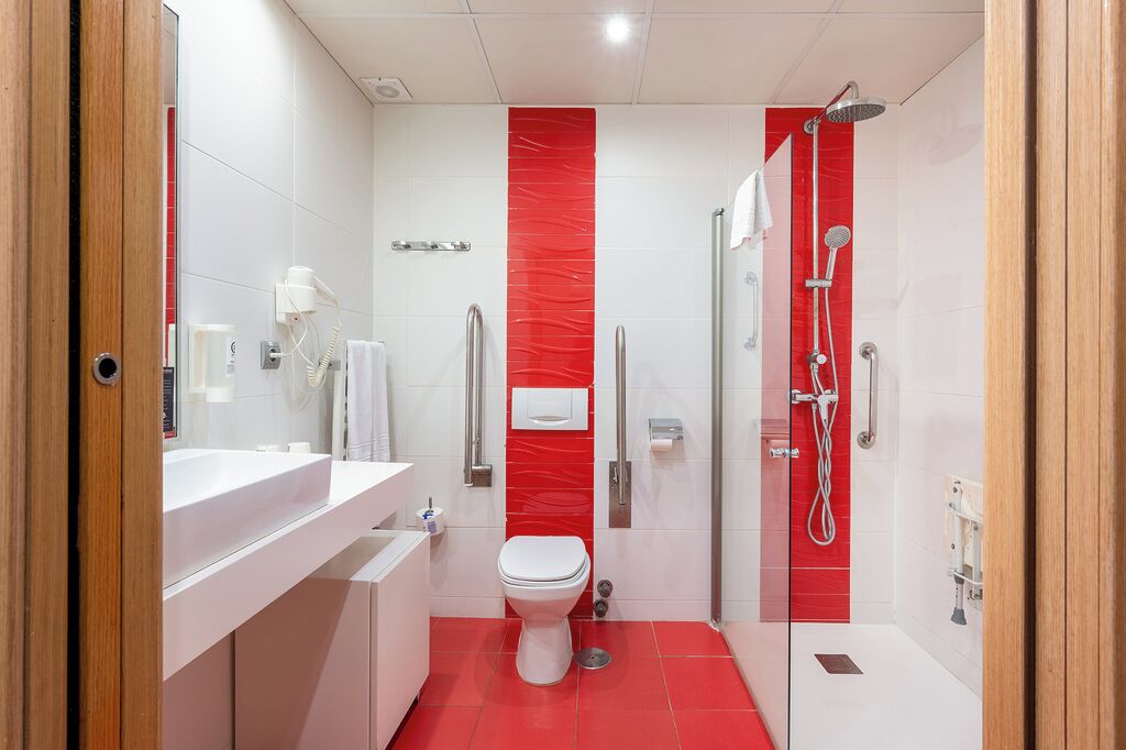 Un baño moderno con un lavamanos blanco, inodoro y zona de ducha con azulejos rojos.
