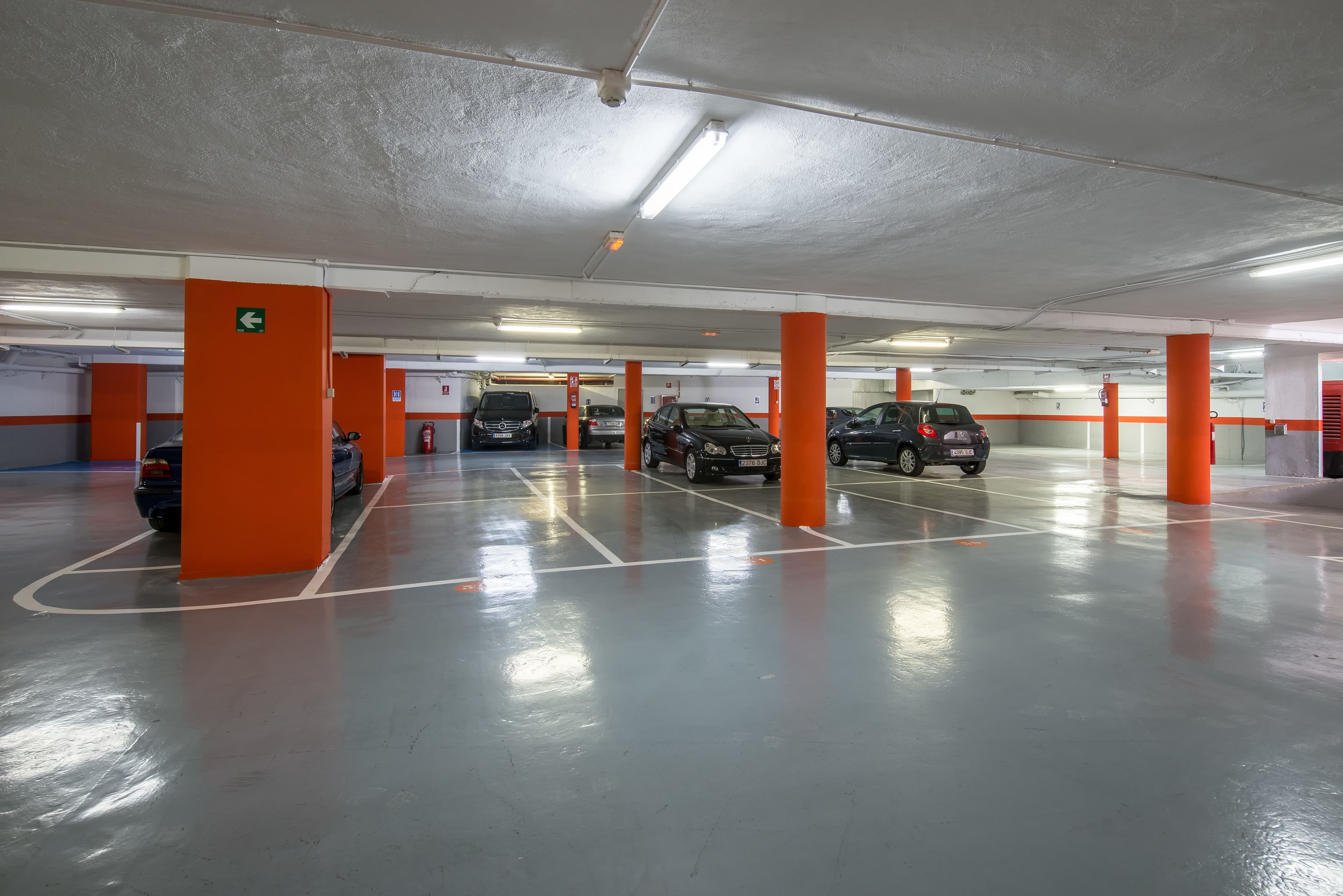 Un parking à plusieurs niveaux, avec des piliers orange, un marquage au sol bien visible et un plafond doté d’un éclairage fluorescent.