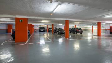 Un estacionamiento de varios niveles con pilares naranja, marcas de carril claras e iluminación fluorescente en el techo.