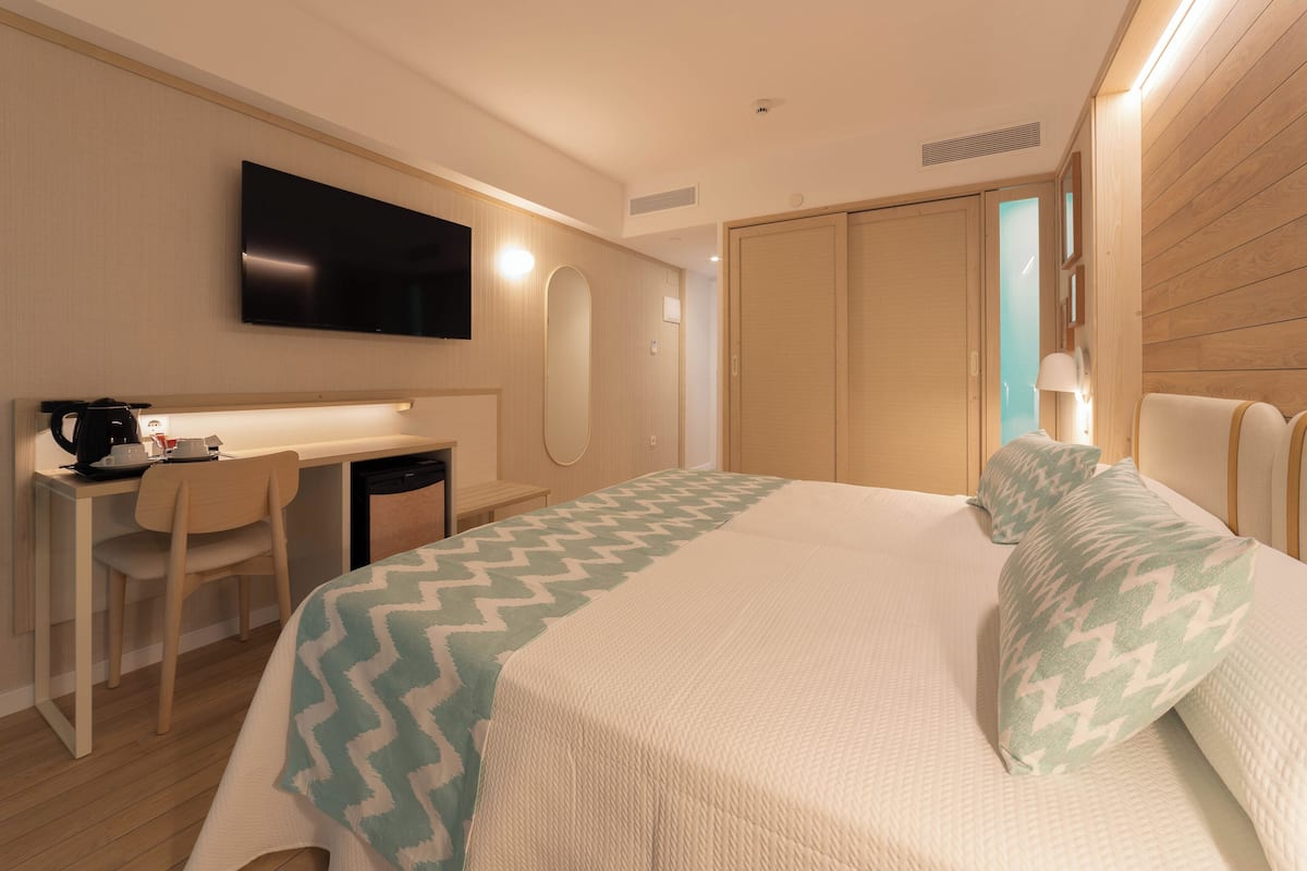 A hotel room with a bed, a desk, a chair, a television, and a wardrobe.