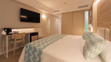 A hotel room with a bed, a desk, a chair, a television, and a wardrobe.