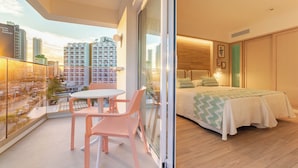 A modern hotel room with a balcony, a bed with a green zigzag bedspread, and a view of high-rise buildings. - Hotel Ambassador Playa I (Benidorm)