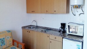 Una cocina compacta con armarios de madera, un fregadero, un microondas y un calentador de agua.