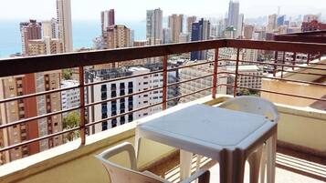 Un balcón con mesa y sillas, con vista a un paisaje urbano de edificios altos y al mar.