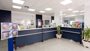 Zona de recepción con mostrador, carteles informativos y plantas en macetas.