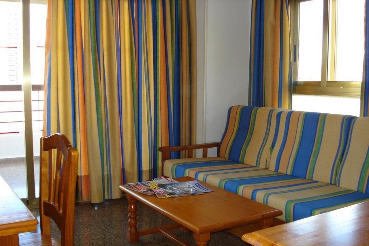 Una habitación con un sofá a rayas, sillas de madera, una mesa de madera y una ventana con cortinas.
