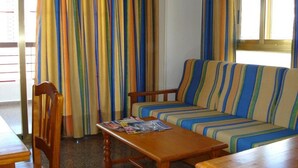 Una habitación con un sofá a rayas, sillas de madera, una mesa de madera y una ventana con cortinas.
