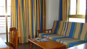 Una habitación con un sofá a rayas, sillas de madera, una mesa de madera y una ventana con cortinas.