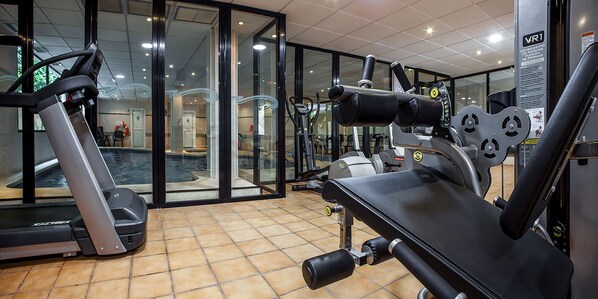 Un gimnasio con equipamiento de ejercicio, una cinta de correr y una piscina visibles a través de puertas de vidrio.
