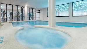 Una piscina interior con agua cristalina, rodeada de equipo de ejercicio y puertas de vidrio que dan a otras zonas.