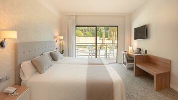 Quarto de hotel com duas camas, uma escrivaninha, televisão e varanda com vista para o verde.