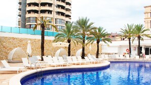 A swimming pool with lounge chairs and palm trees, surrounded by stone walls and a building in the background. - Hotel Agua Azul - Adults Only (Benidorm)