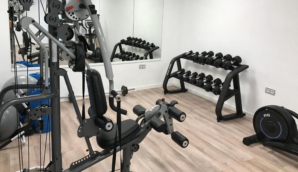 Un gimnasio con equipos de ejercicio variados, incluyendo mancuernas en estanterías y una máquina de pesas.