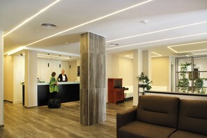 A hotel lobby with a reception desk, a large pillar, a seating area, and a reception counter. - Alameda (Benidorm)