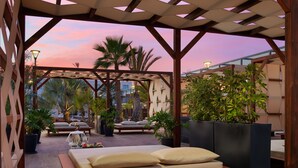A covered outdoor seating area with a wooden bench, lounge chairs, and potted plants. - H10 Ocean Dreams Boutique Hotel - Adults Only (La Oliva)