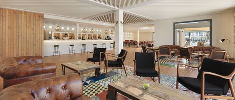 A spacious lobby with leather sofas, wooden tables, and a bar area with stools.
