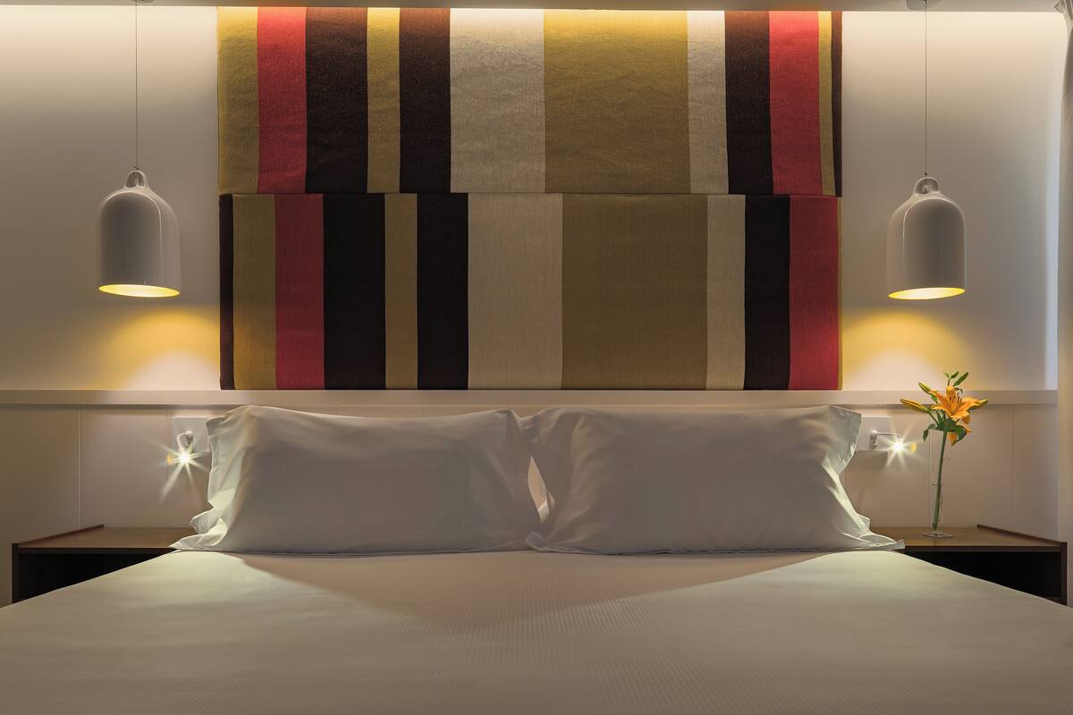 A neatly made bed with white linens, two bedside tables with lamps, and a wall with a striped fabric design.