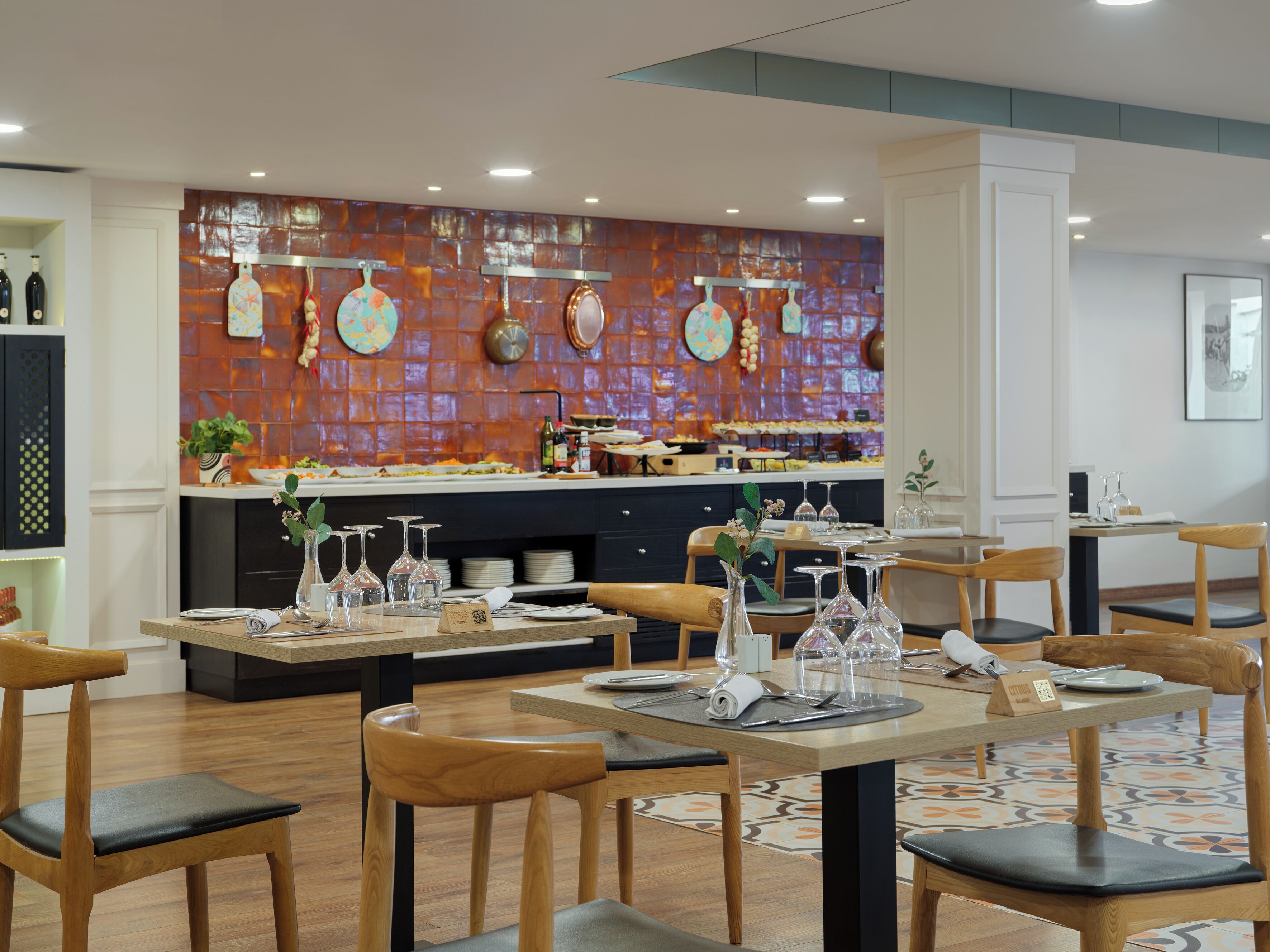 Un restaurante con mesas y sillas de madera, un salpicadero de azulejos y una zona de bufé al fondo.