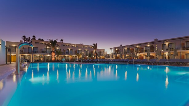 A swimming pool with lounge chairs and umbrellas, surrounded by modern buildings with balconies and outdoor seating. - H10 Ocean Dreams Boutique Hotel - Adults Only (La Oliva)
