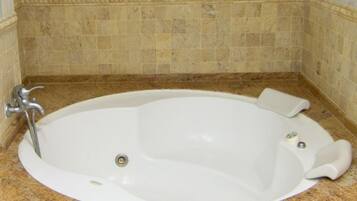 A white bathtub in a corner with a granite countertop and a tiled wall.