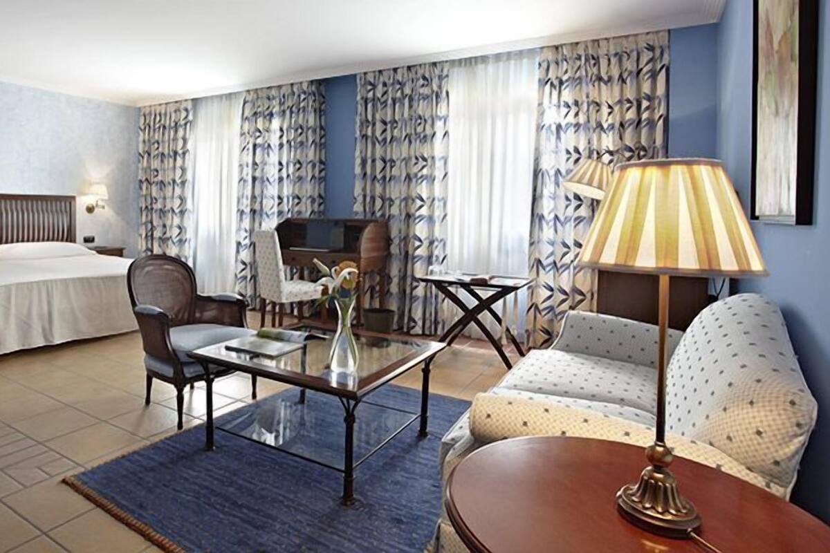 Une chambre d’hôtel avec un lit, un bureau, une chaise, un canapé et une lampe.