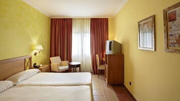 Een hotelkamer met twee bedden, een bureau met televisie, een stoel, een klein tafeltje en een lamp.