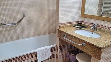 Un baño con bañera, lavamanos con espejo y barra de apoyo.