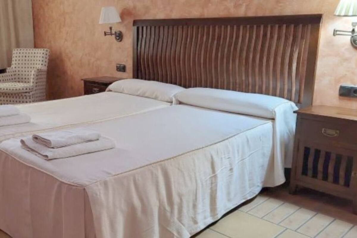 Une chambre double avec deux lits, une chaise, une table de chevet et une lampe.
