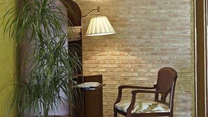 Un hall con pared de ladrillo, una planta en maceta, una silla de madera y una lámpara de pie.