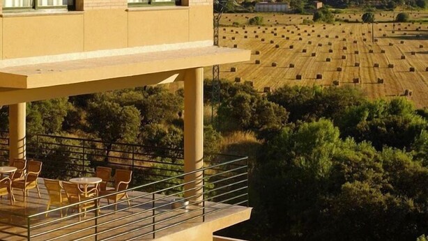 Un edificio con balcón que da a un campo de fardos de heno.