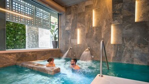Un espace dédié à un bain à remous, agrémenté d’un mur en pierre, d’une fenêtre donnant sur un paysage verdoyant et d’un élément décoratif aquatique.
