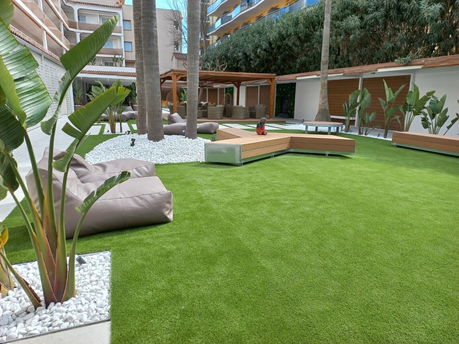 A modern outdoor lounge area with artificial grass, seating arrangements, and potted plants.