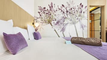 A hotel room with a bed, pillows, a wall-mounted lamp, and a floral mural.