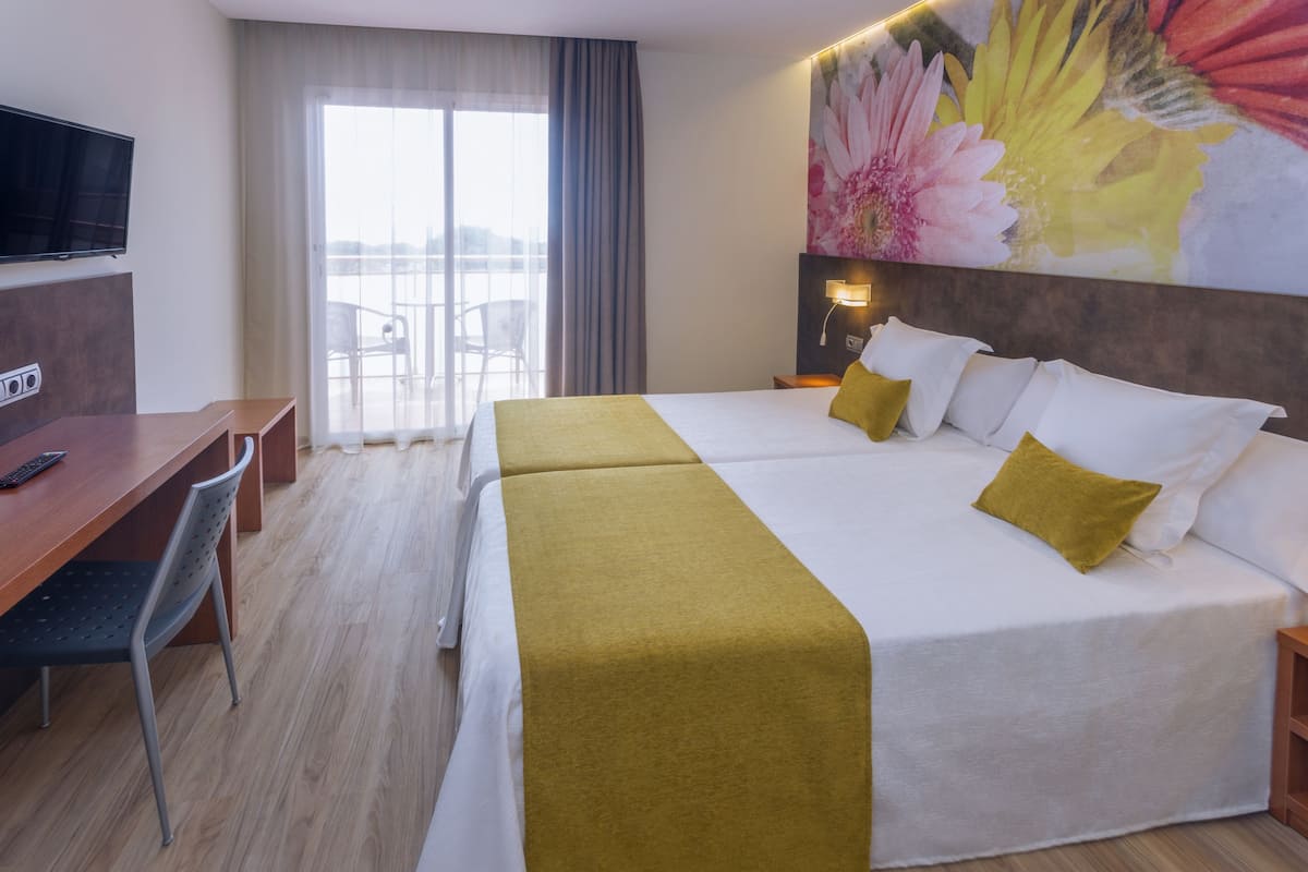 Habitación de hotel con cama, escritorio, silla, televisión y un gran ventanal con cortinas.