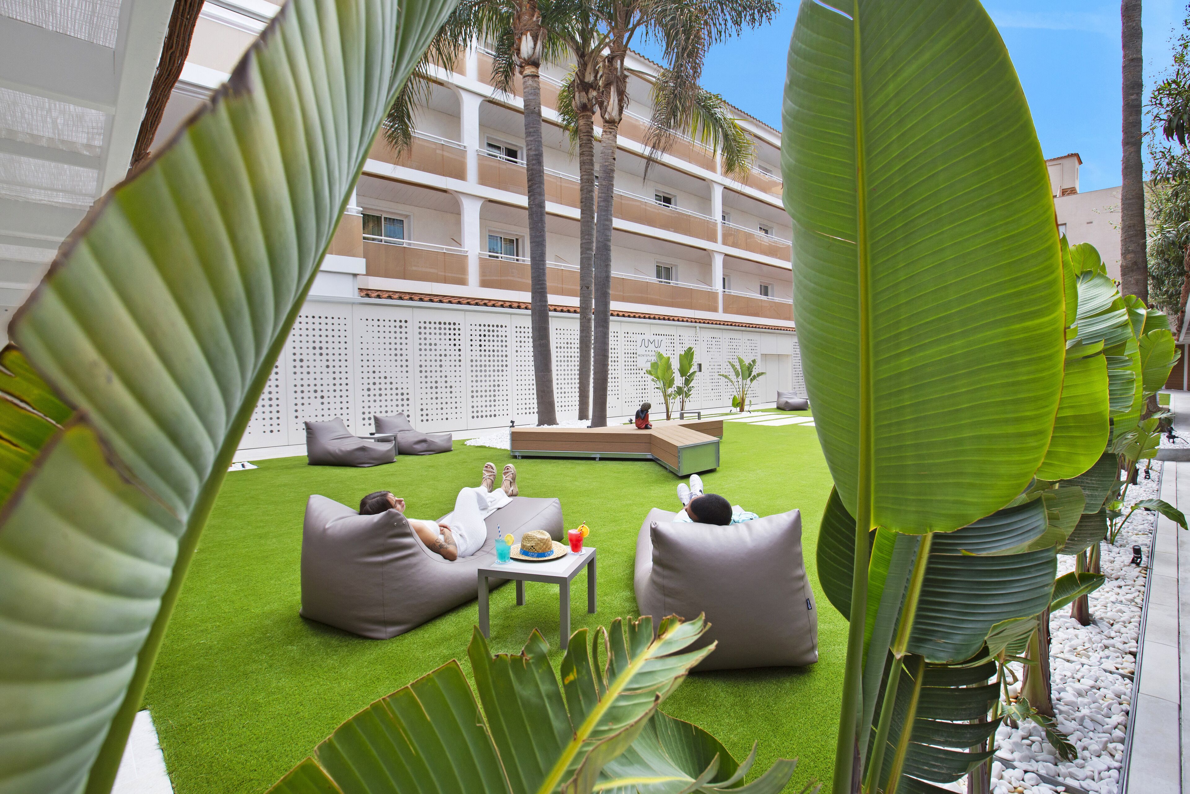 A courtyard with artificial grass, seating areas, and a central table with drinks.